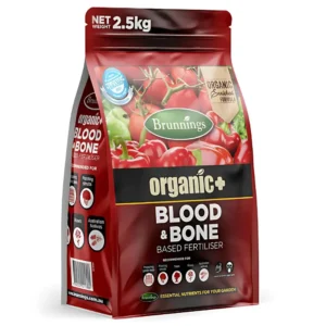 Brunnings Blood & Bone fertiliser bag placed in a garden setting near flowering plants.