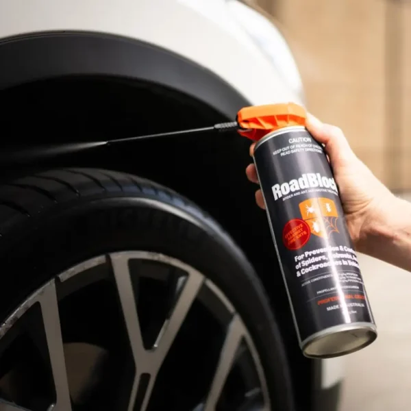 Hand spraying RoadBlock Spider and Ant Automotive Treatment 350g around a car wheel arch for targeted pest protection.