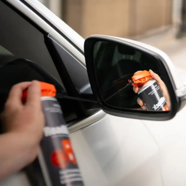 Hand spraying RoadBlock Spider and Ant Automotive Treatment 350g near a car side mirror to prevent pests.