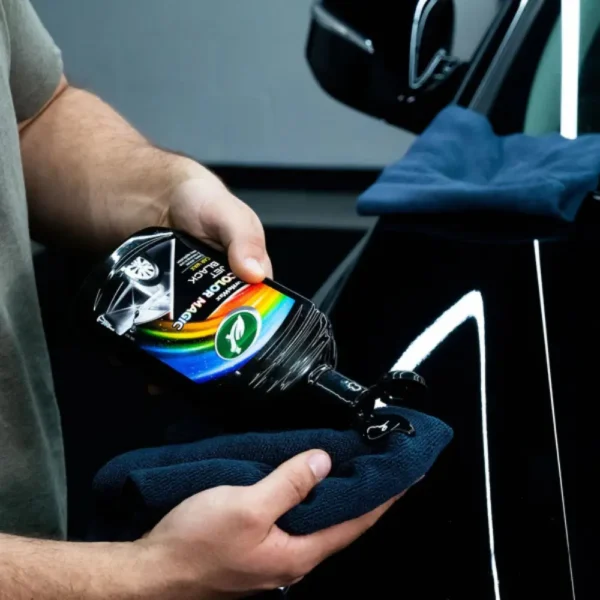 Person applying Turtle Wax Color Magic Jet Black Wax FG52708 500ml onto a microfiber cloth for car detailing