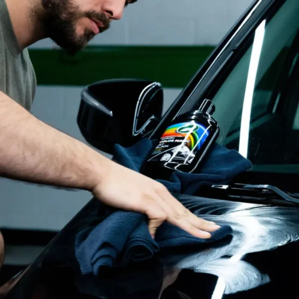 Person spreading Turtle Wax Color Magic Jet Black Wax FG52708 500ml evenly on a black car with a microfiber cloth.