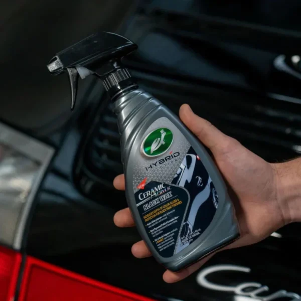 Turtle Wax Hybrid Solutions Ceramic Acrylic Black Wax 473ml next to a clean black car panel mid-application on white background