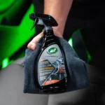 Turtle Wax Inside Job 473ml next to a microfibre cloth and a clean car dashboard on white background
