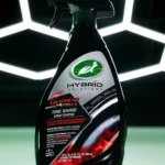Close up of Turtle Wax Hybrid Solutions Graphene Tyre Shine 680ml bottle against background with hexagon lighting grid.